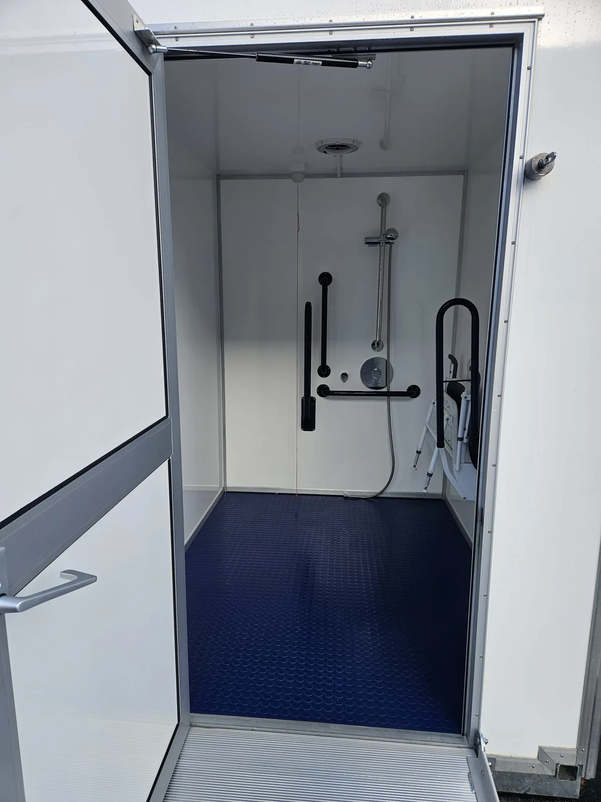 Accessible shower pod interior with grab rails and fold-down shower seat